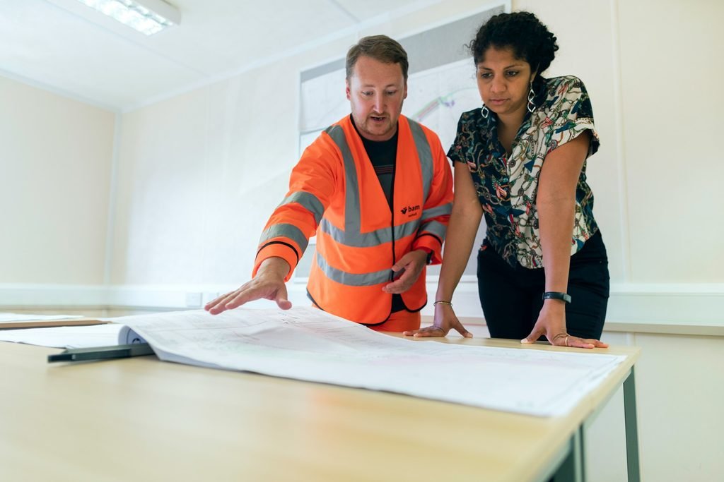 Profesional de reformas revisando planos con cliente en oficina, destacando la colaboración en proyectos de construcción.