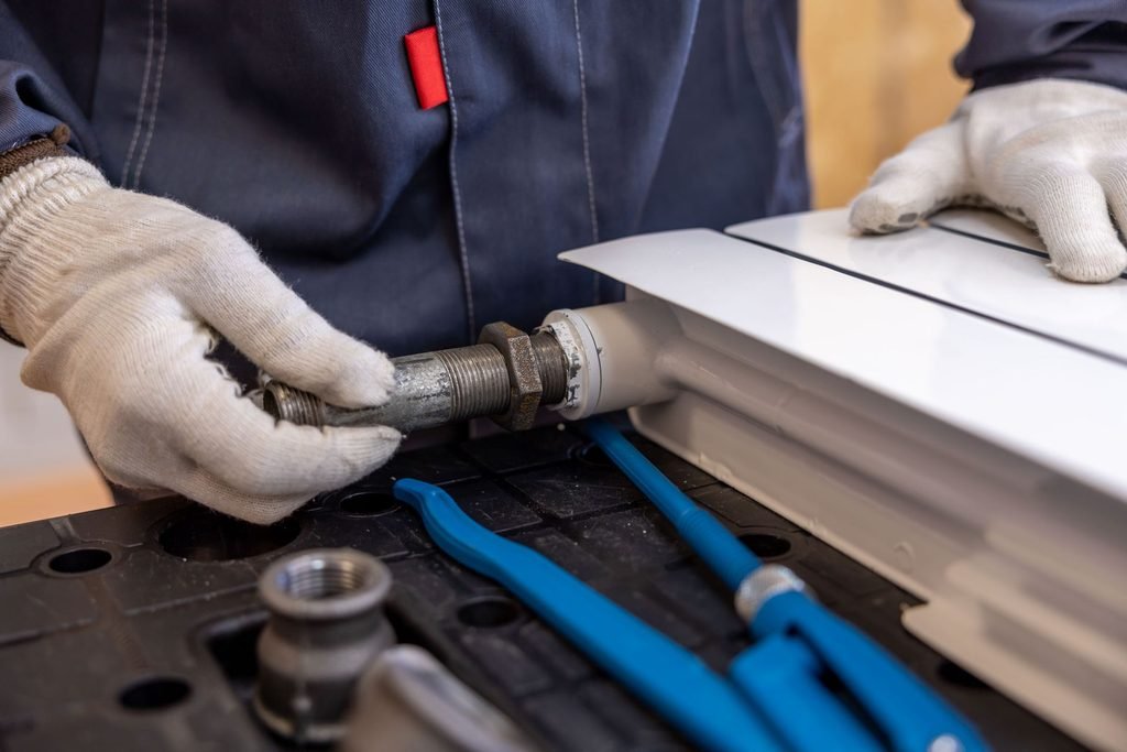 Técnico ajustando una conexión de calefacción con herramientas en un taller.